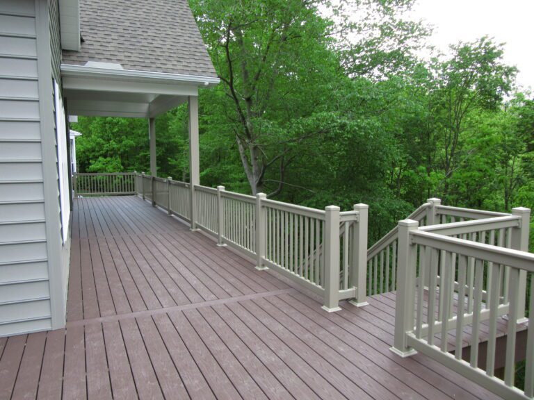 Clay-colored vinyl deck railings surround a deck with green trees in the background.