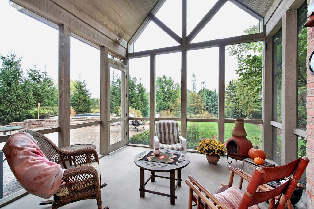 A screened-in porch with wicker furniture, pumpkins, and mums for fall.