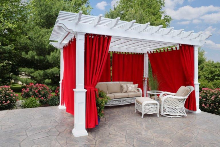 A large white pergola with red drapes around it and a sofa and chair under it.